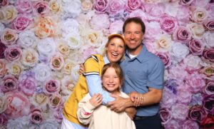 Family smiling at a Glam Photo Booth in front of a floral backdrop at a charity gala event