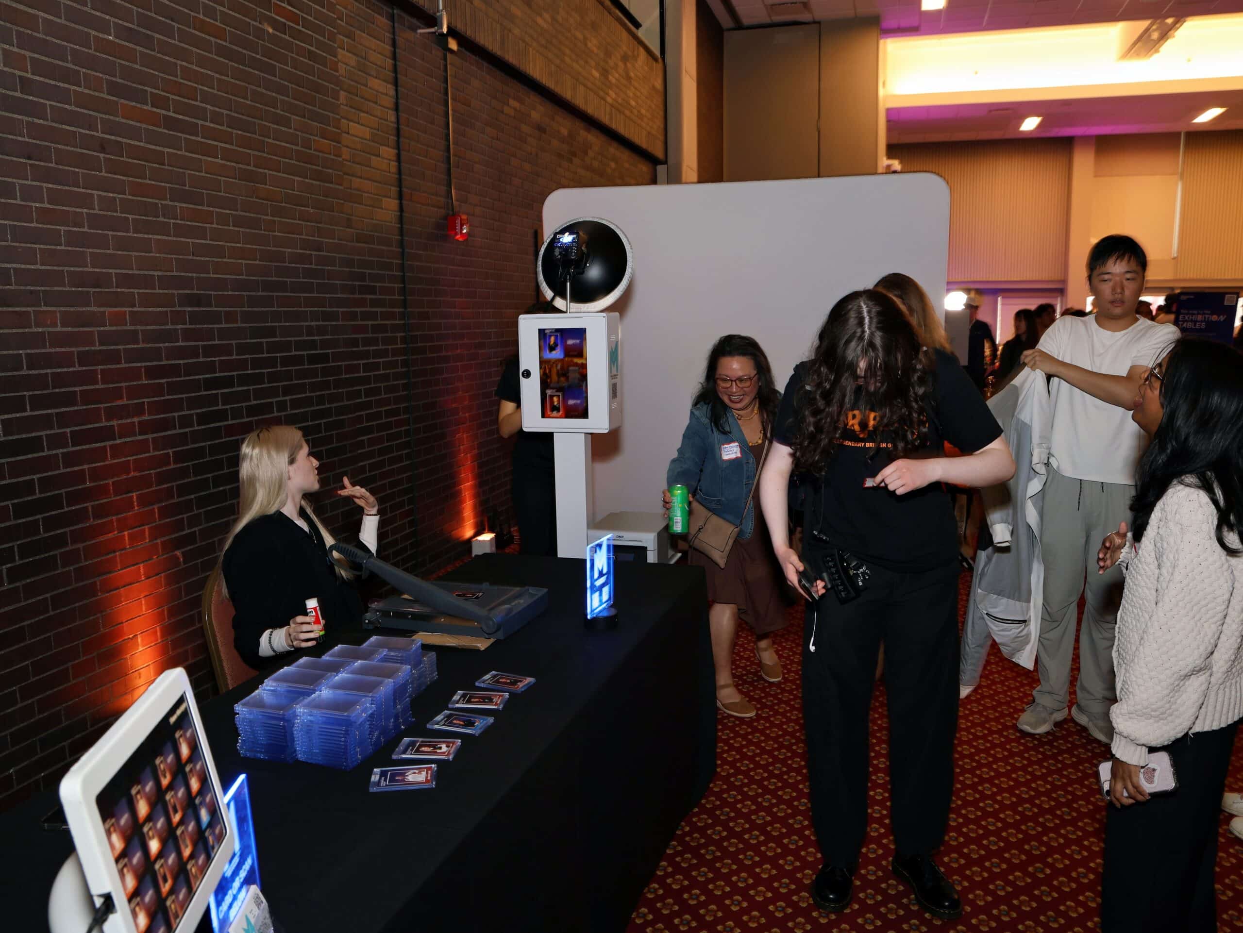 Interactive photo booth setup at an event, featuring a staff member assisting guests, with a sleek photo display and printed photo cards, enhancing the celebration experience.
