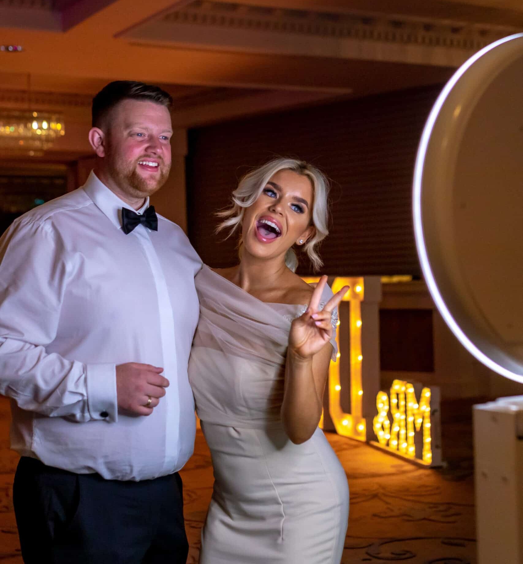 Couple laughing and posing in front of the Selfie Station Luxe photo booth at an evening event
