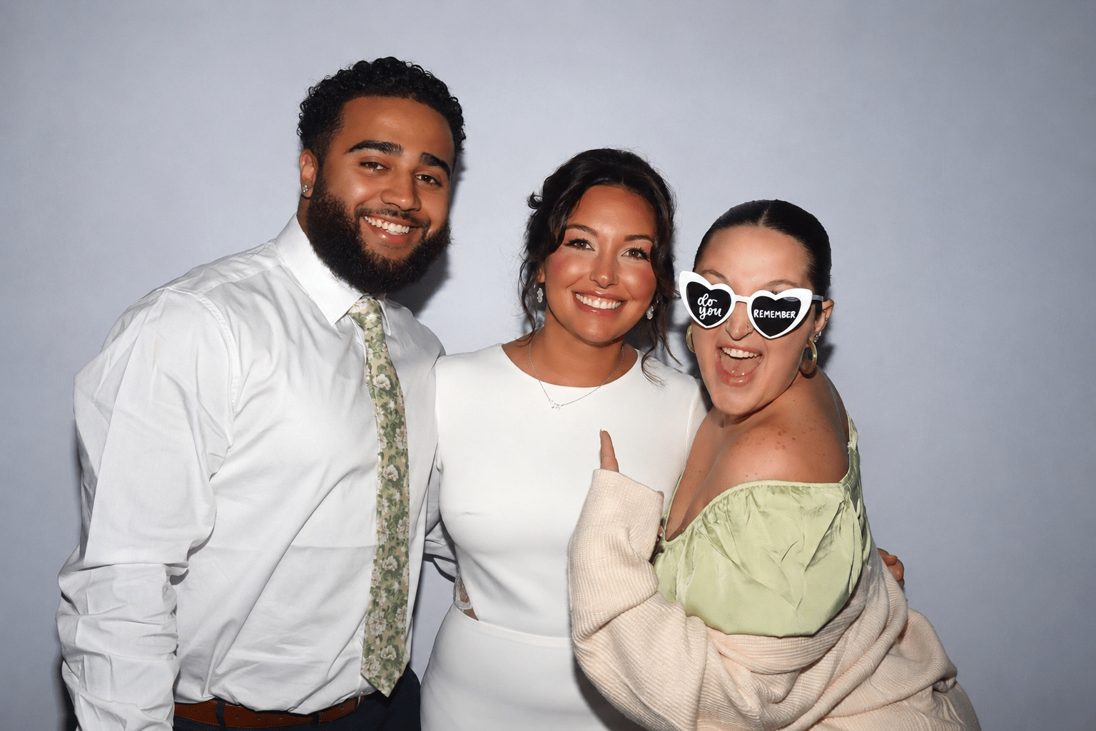 A fun wedding photo booth moment featuring three guests celebrating with playful props and big smiles.