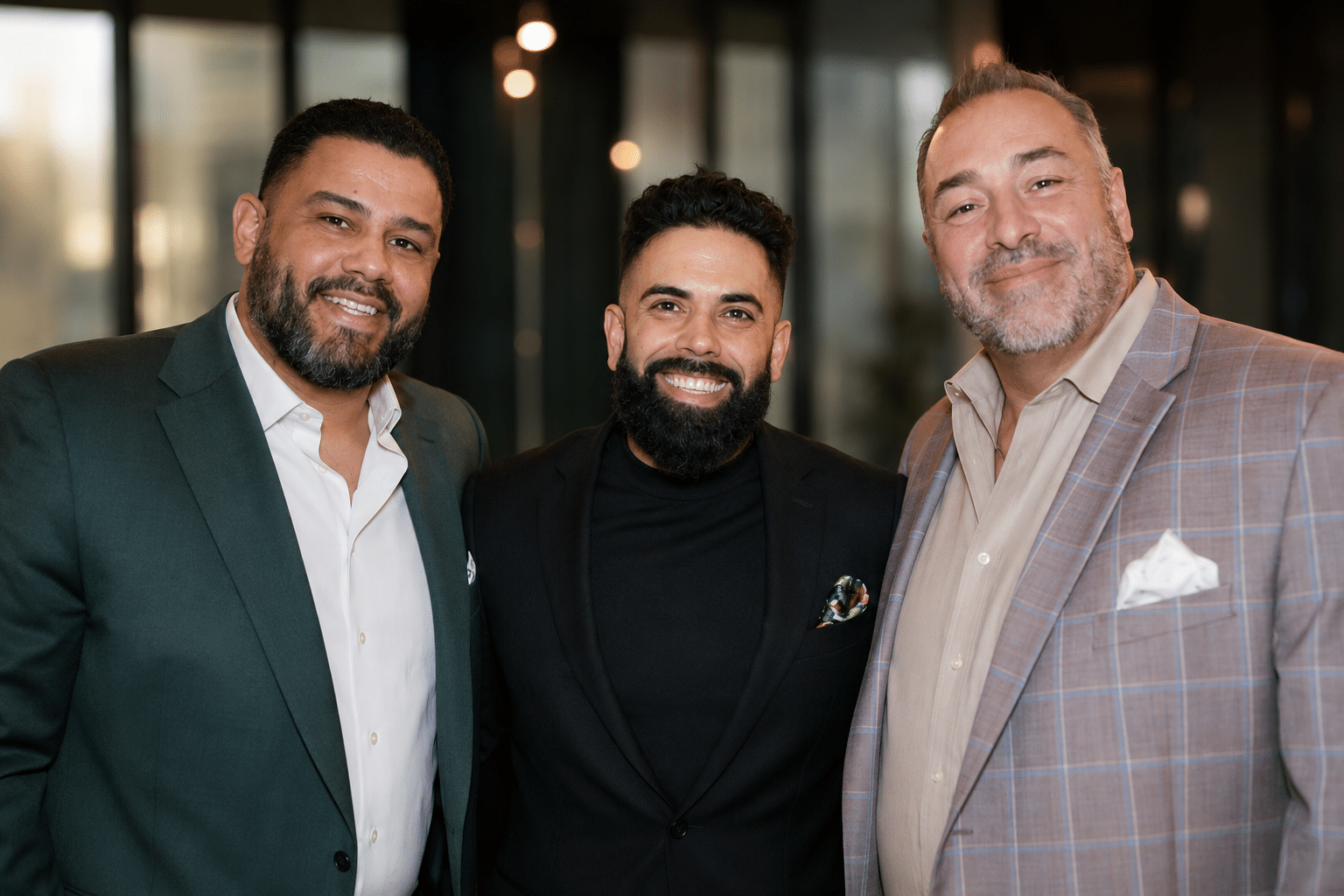Three men smiling together in a modern event space, showcasing a friendly atmosphere, representing engaging guest experiences at AI headshot photo booths.