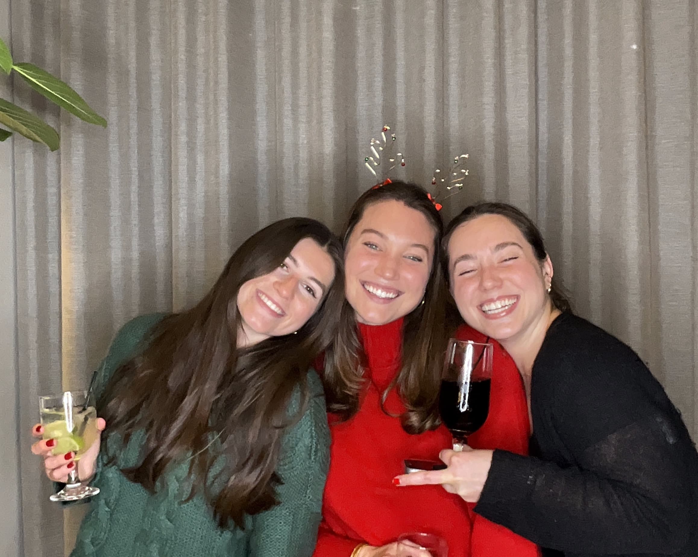 Three smiling guests enjoying drinks and festive headwear at a Magic Mirror of New England photo booth.