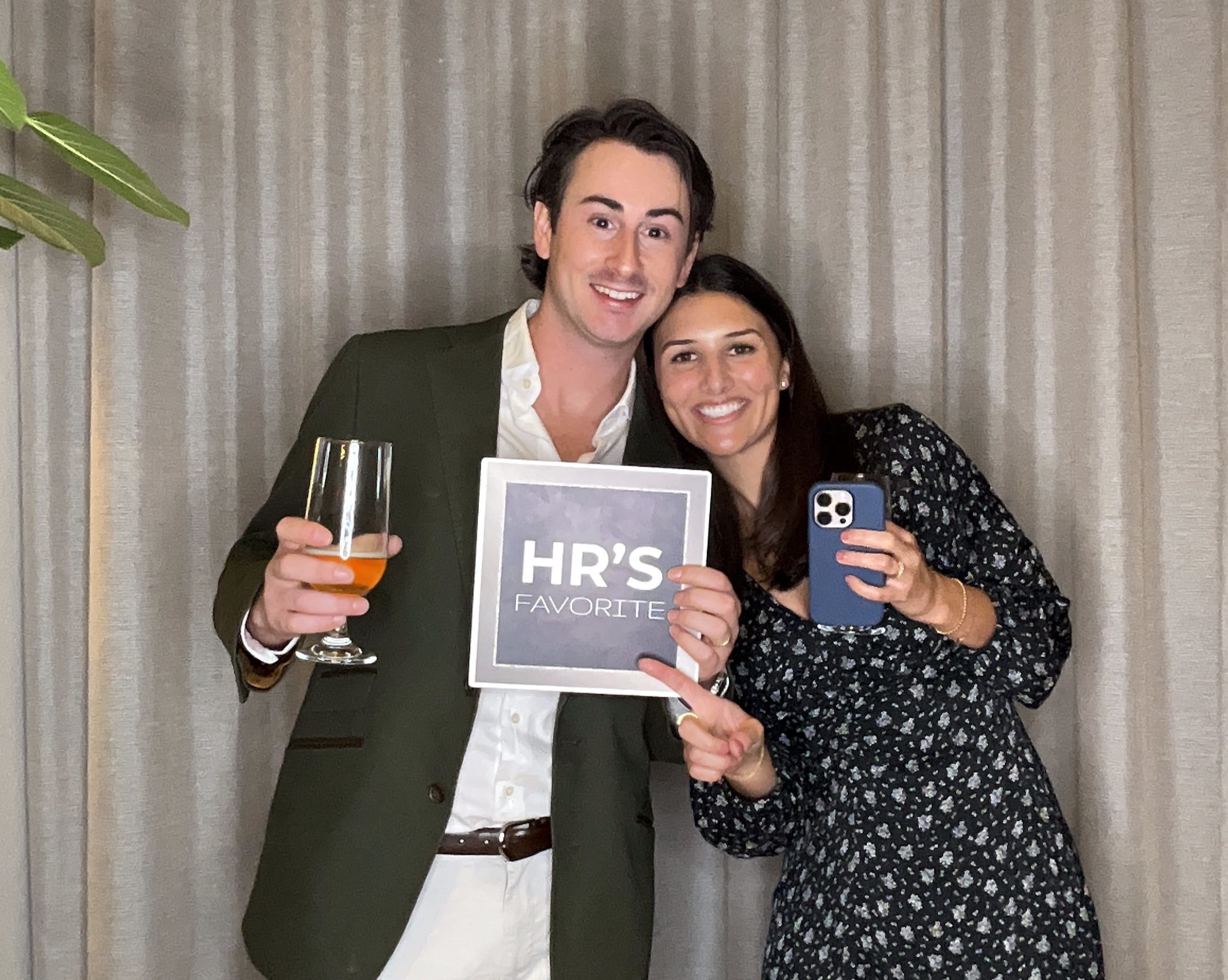 Couple posing with custom photo booth sign and phones at corporate event.