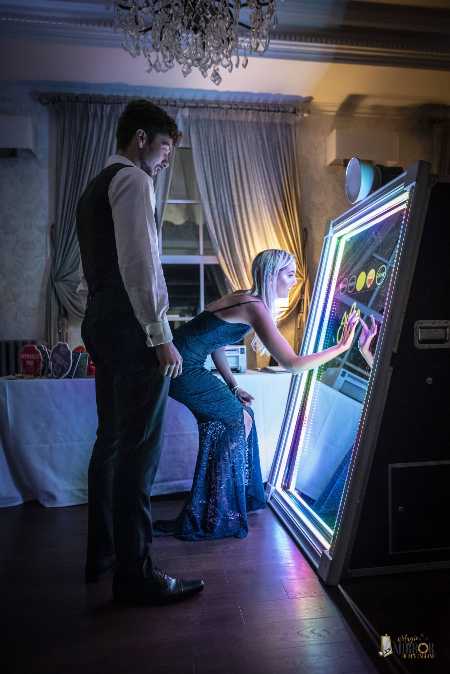 Guests using the touch screen on a Magic Mirror photo booth with rainbow LED frame at an evening event in NH