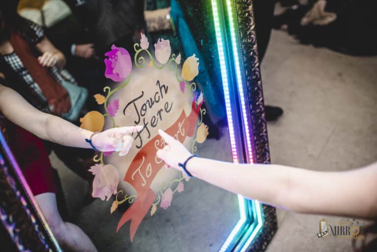 Guests tapping the Touch Here prompt on a Magic Mirror photo booth screen with a rainbow LED frame