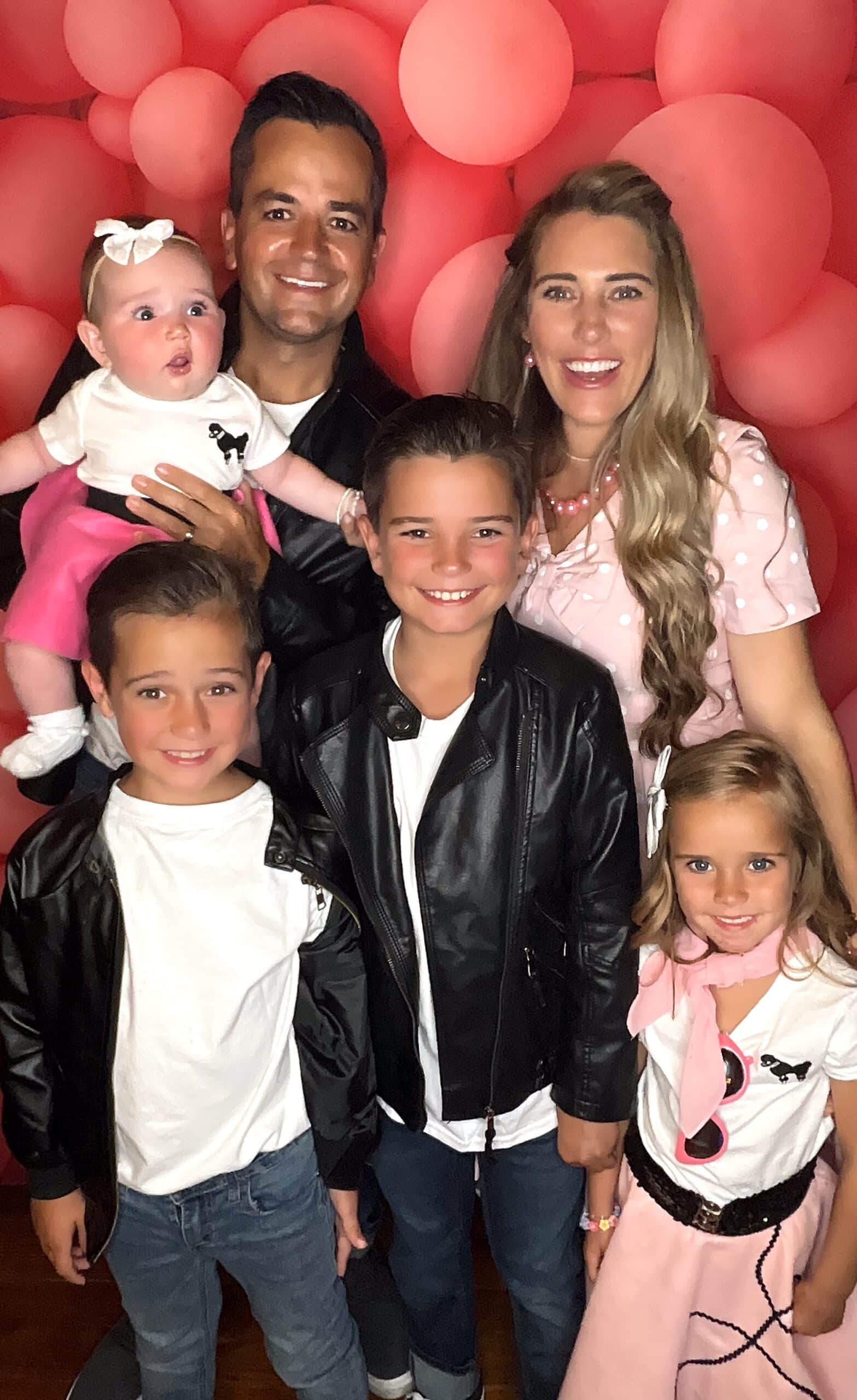 A family with a baby and three children posing in front of a pink balloon wall at a Dream Booth photo booth