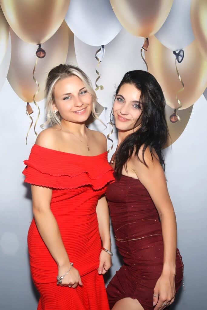 Two women in red dresses posing in front of a balloon backdrop at a birthday party with the Selfie Station Luxe