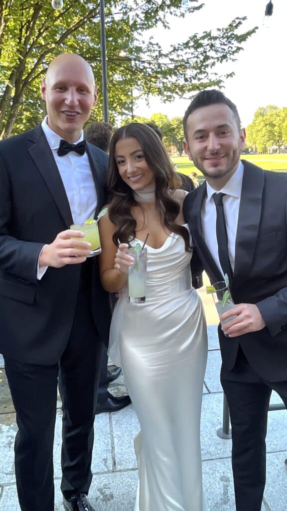 Guests in black tie and a white satin gown holding cocktails on the lawn at an outdoor wedding cocktail hour in NH