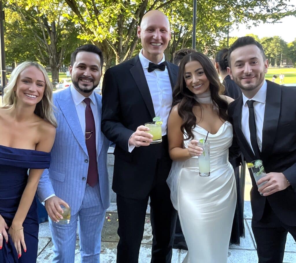 Group of wedding guests in black tie holding cocktails outdoors at a cocktail hour with a roaming photo booth in NH