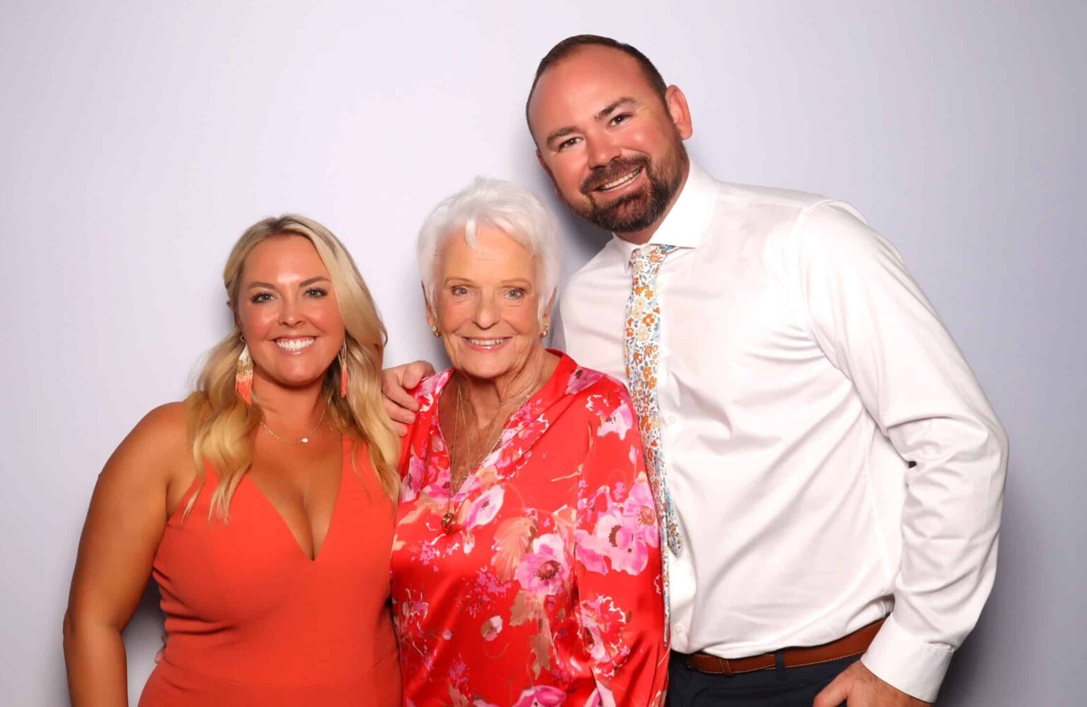 Three guests posing together, including an older woman in a floral dress, in front of a light backdrop