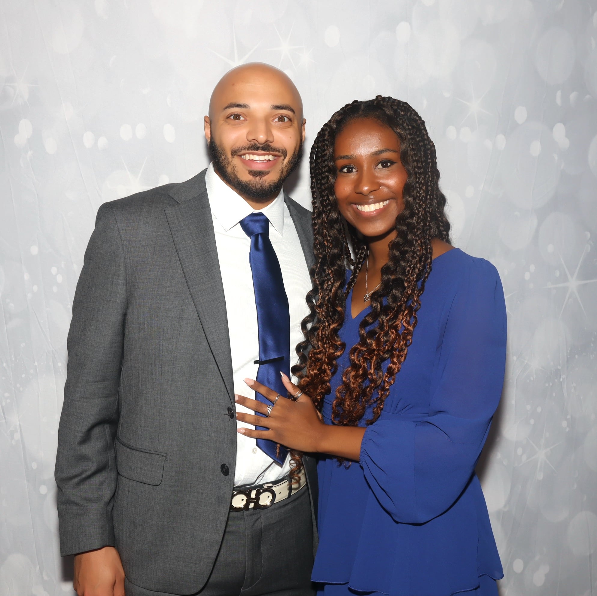 Couple posing together at a photo booth event with a silver sparkle backdrop
