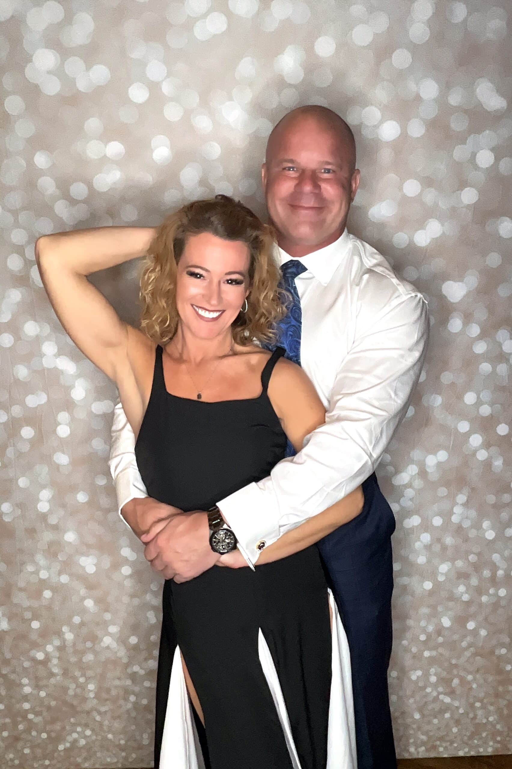 Couple posing together at a holiday party photo booth with a sparkle backdrop