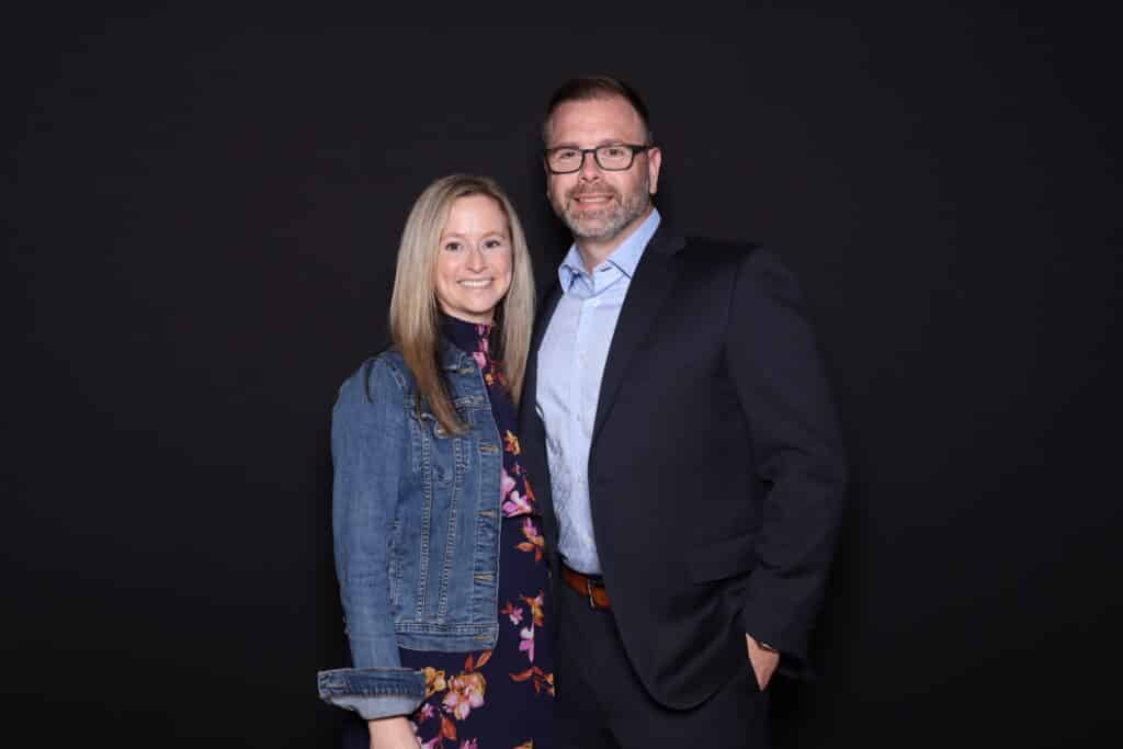Man and woman in smart casual attire posing together in a studio photo booth with a black backdrop at a corporate event