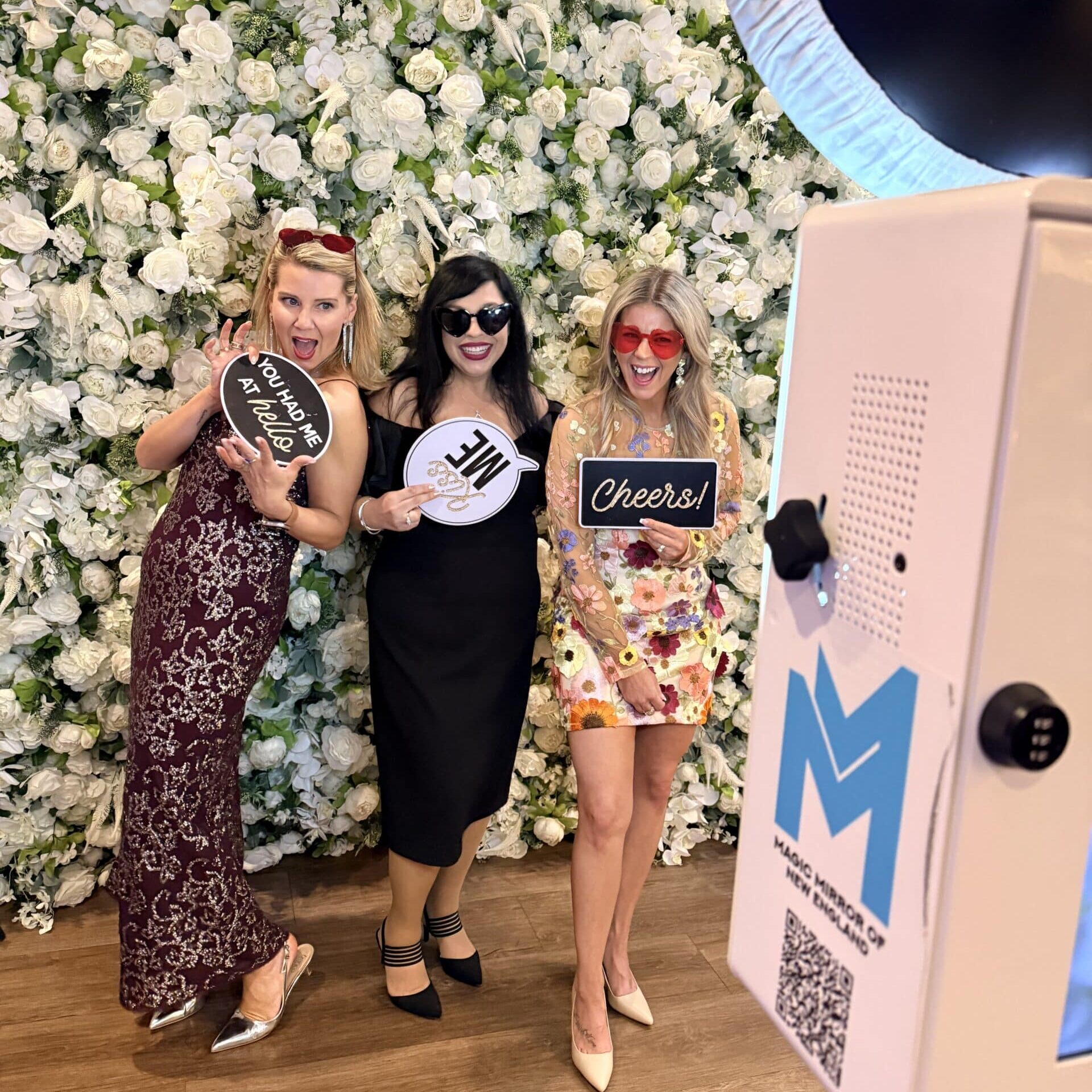 Two wedding guests posing next to a studio photo booth with GLAM in front of a floral wall at LaBelle Winery in Derry, New Hampshire