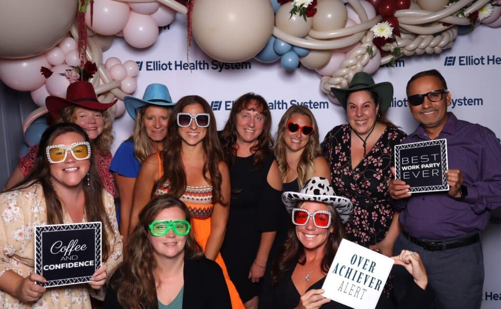 Large team in sunglasses and hats posing with props at the photo booth at a Manchester NH celebration