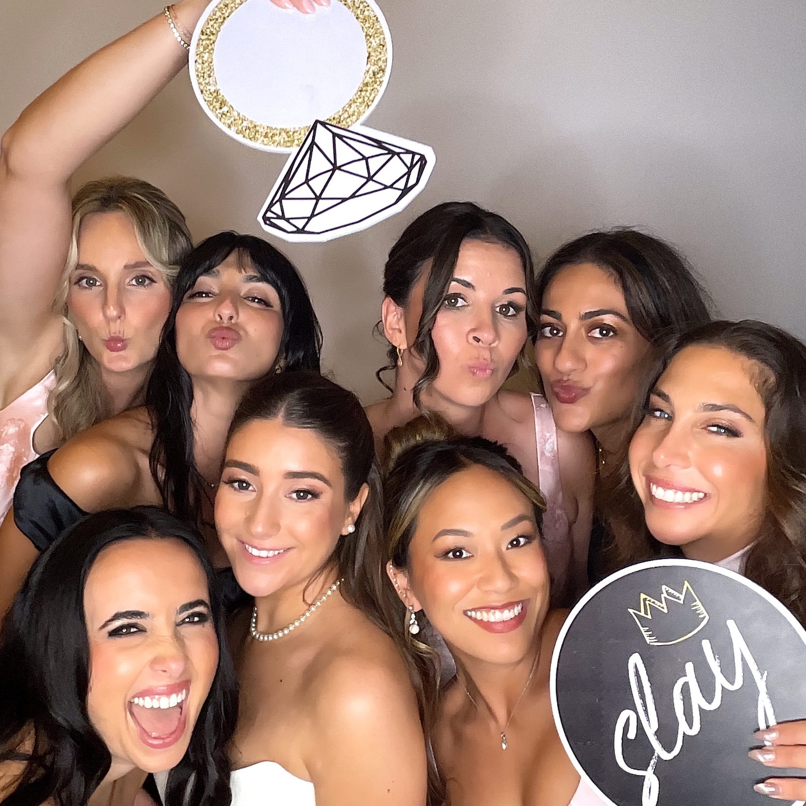 A group of bridesmaids in pink and black blowing kisses and holding diamond ring and Slay prop signs