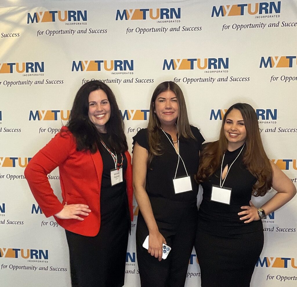Three guests in black outfits and a red blazer posing at a corporate event backdrop