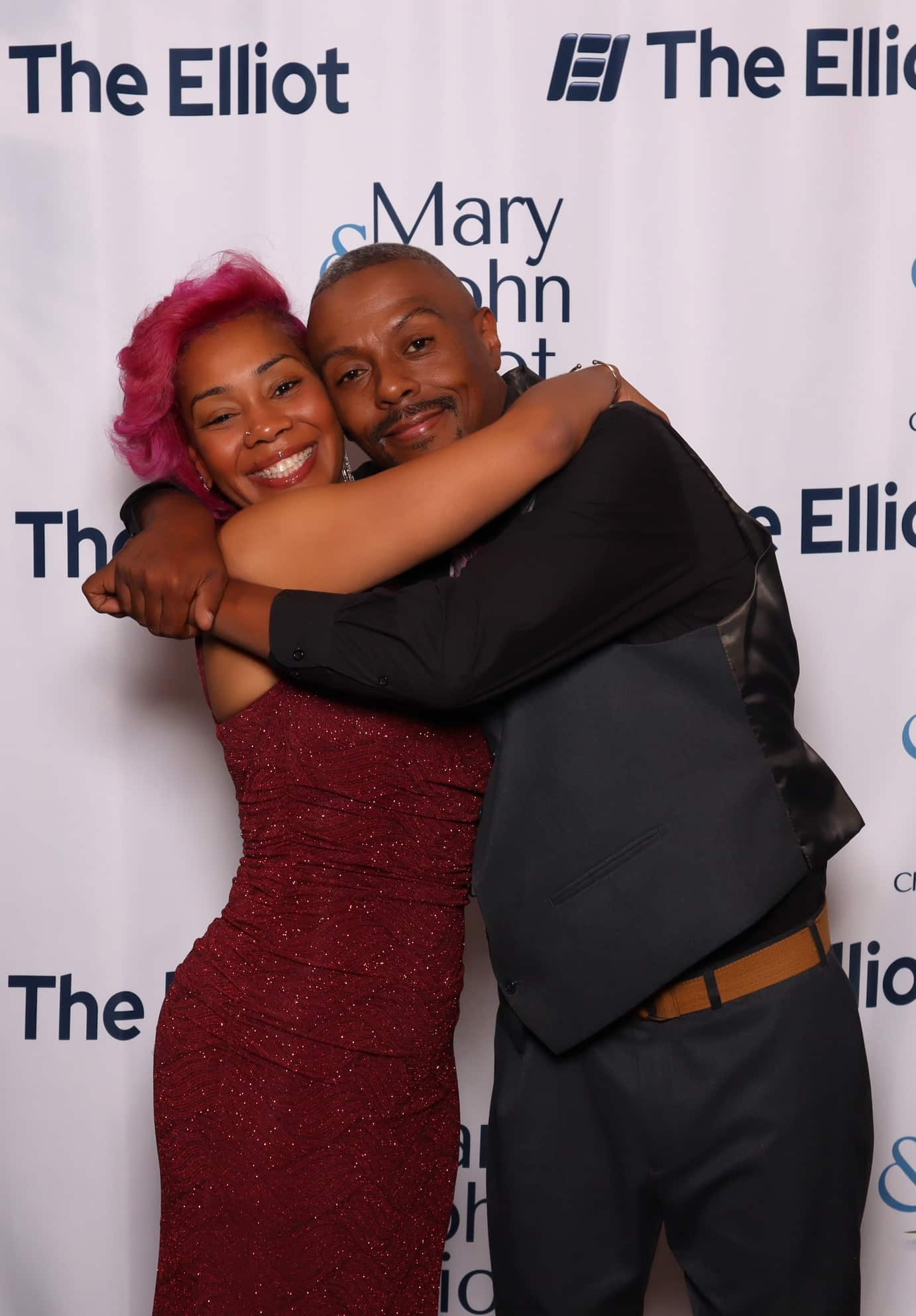 Two guests hugging in front of The Elliot backdrop at the Elliot Health System Gala photo booth