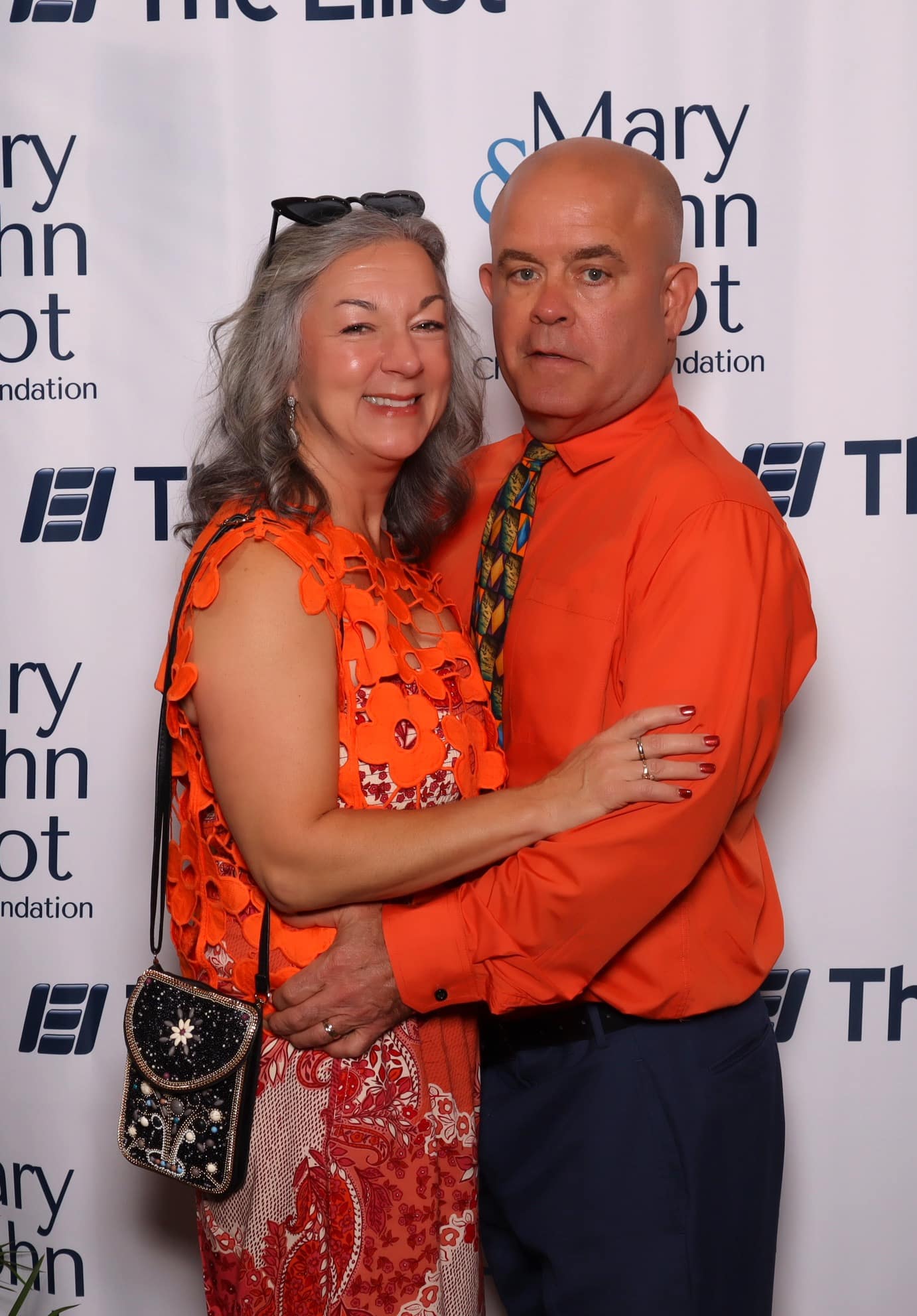 Couple in orange outfits pose at the Elliot Health System Gala photo booth