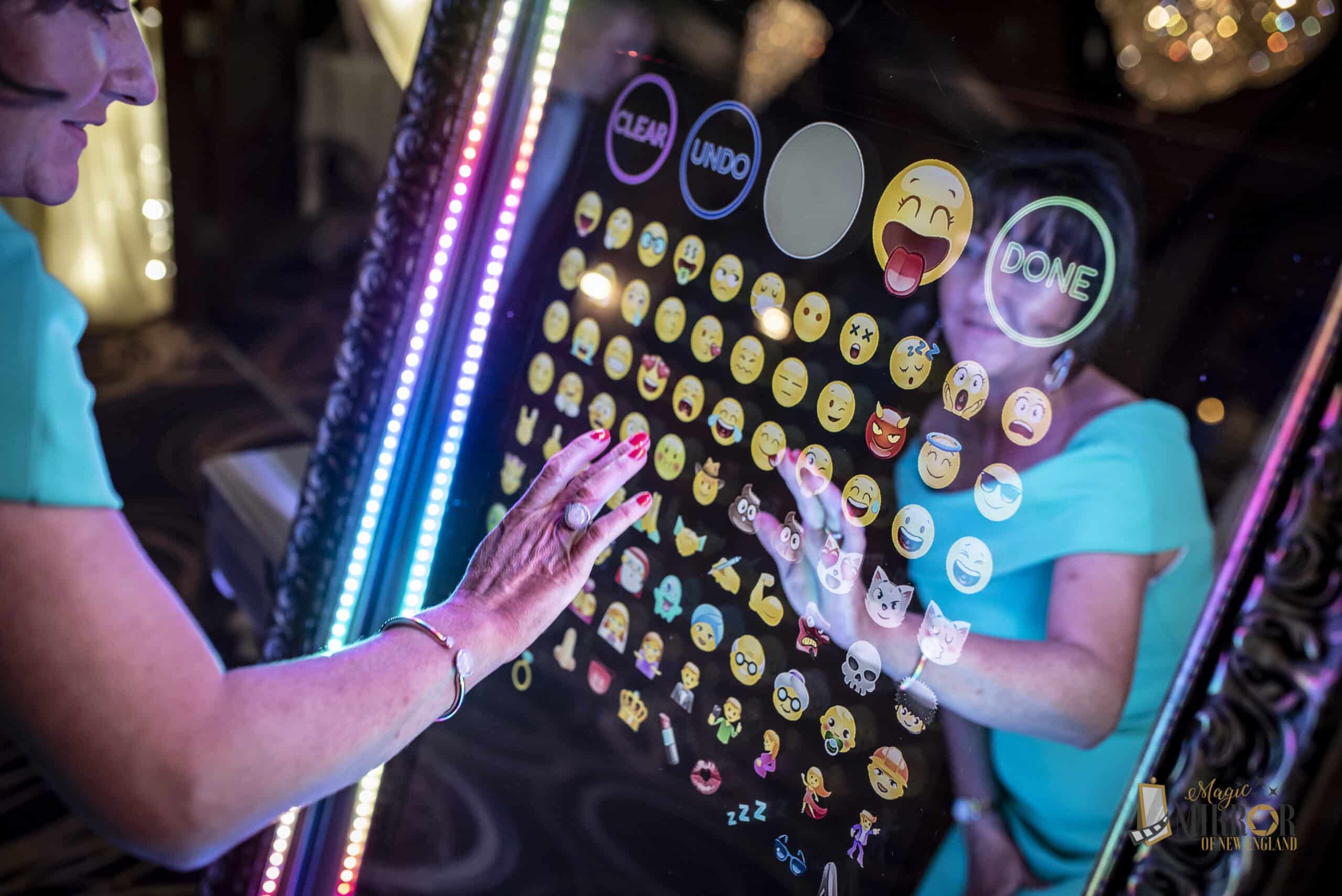 Guests tapping emoji reactions on the Magic Mirror photo booth touch screen with rainbow LED frame