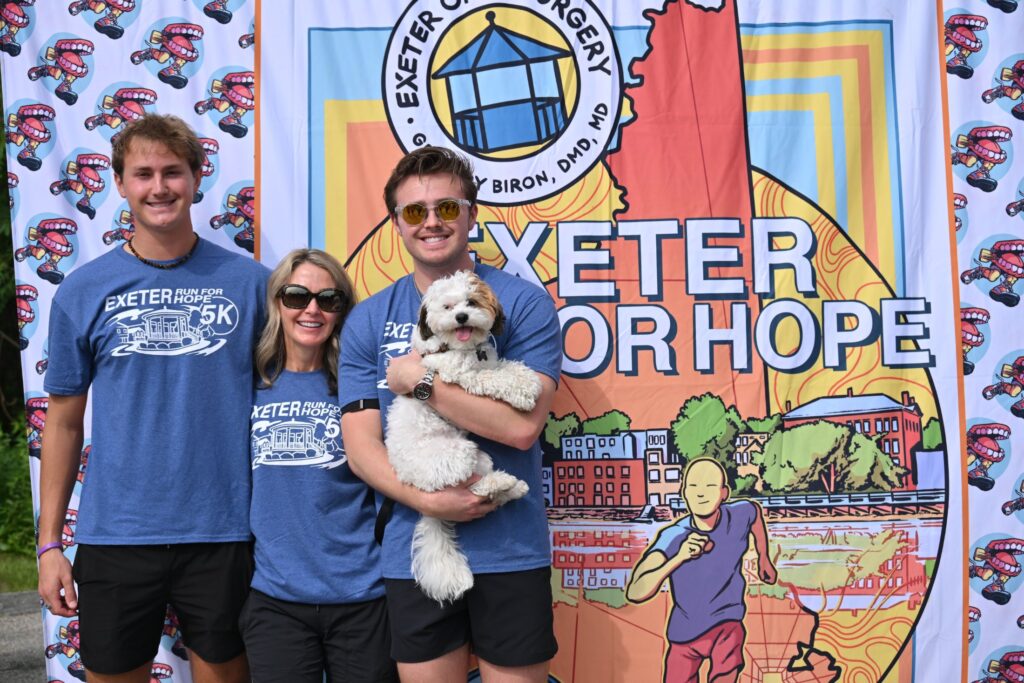 Family with a small dog posing in front of the Exeter Run for Hope photo backdrop