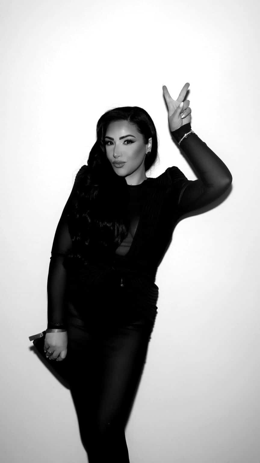 Black and white GLAM booth portrait of a woman in a sheer black outfit making a peace sign at a New England gala