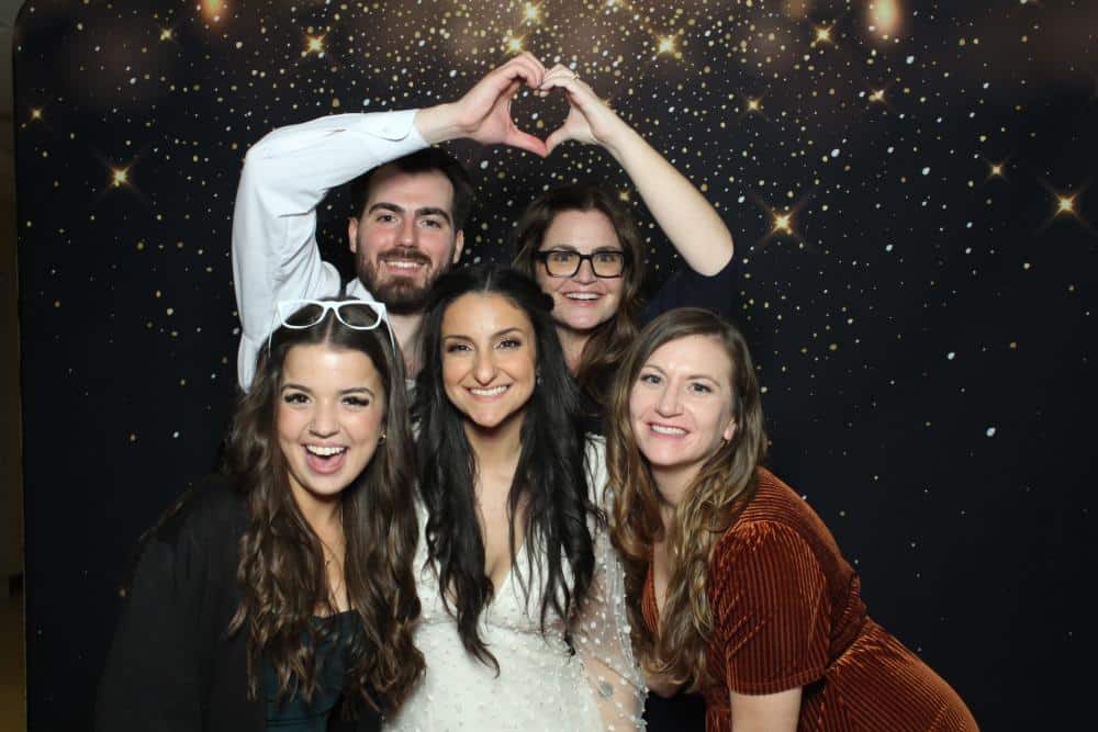 Five wedding guests making a heart with their hands in front of a starry night photo booth backdrop