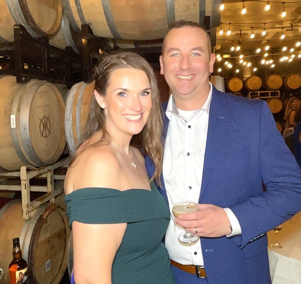 Couple posing in front of stacked wine barrels and string lights at a LaBelle Winery wedding cocktail hour, roaming photographer photo in NH