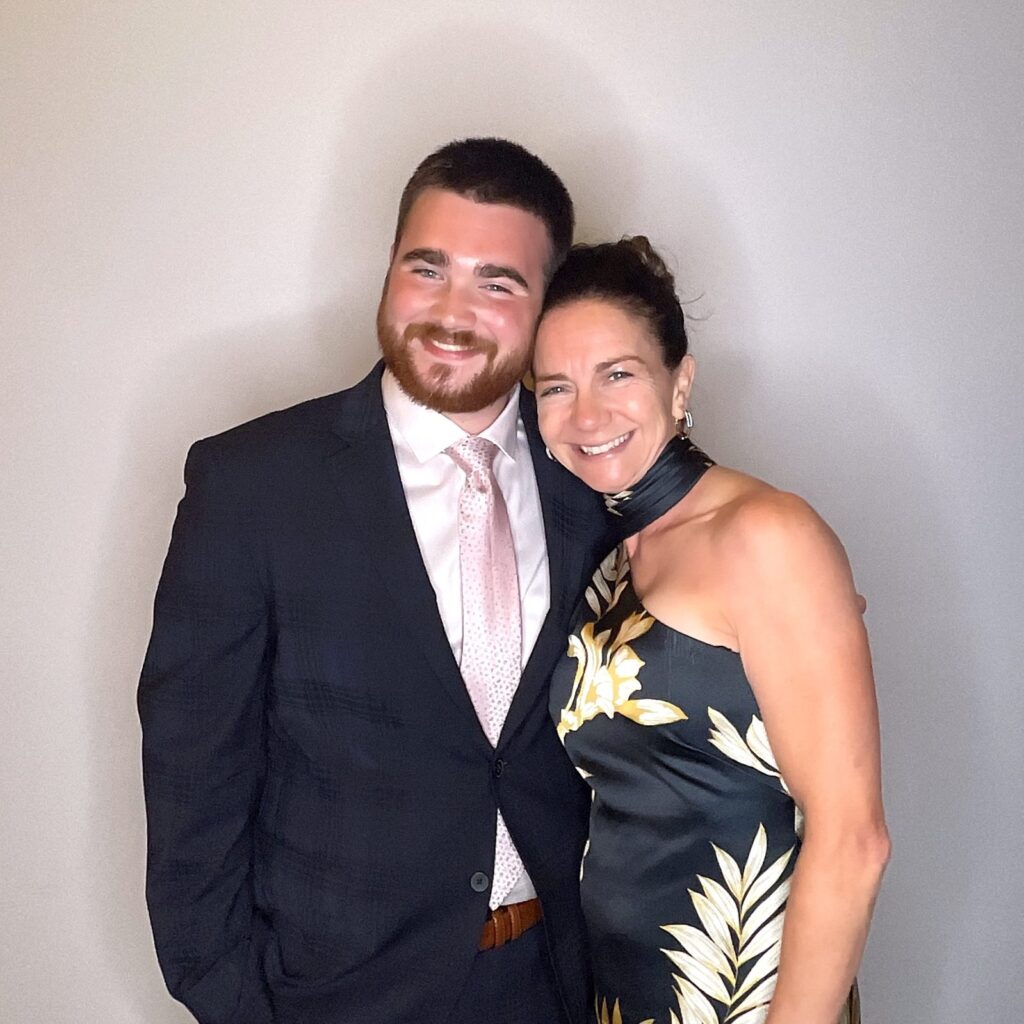 A man in a navy suit and a woman in a floral dress smiling together at a wedding